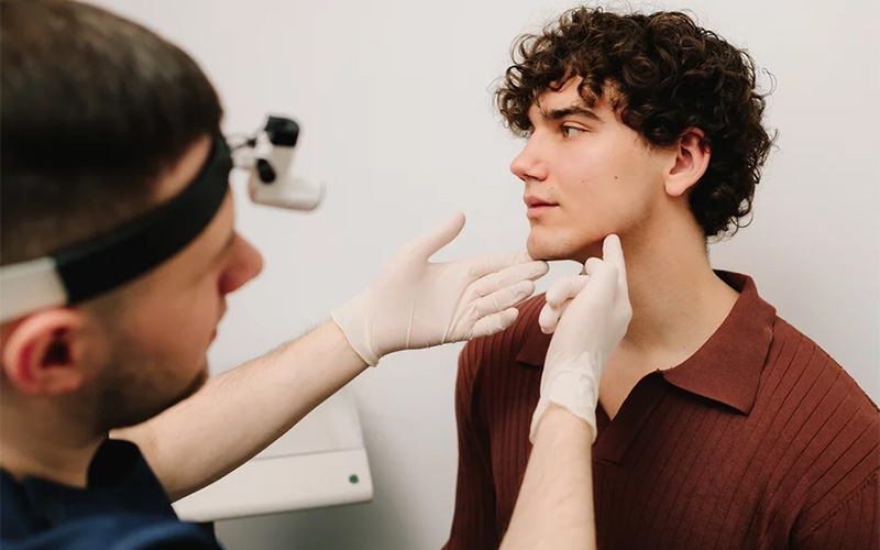 Face correction and lifting to reshape chin. Facebuilding. Doctor touching male face in protective gloves before chin shape correction with fillers.