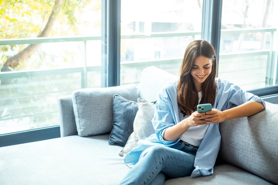 Young girl seated on the couch, smiling while checking her smartphone